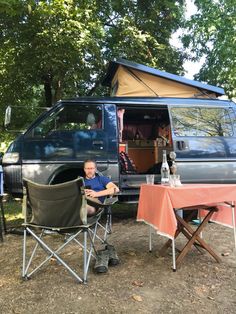 a man sitting at a table in front of a camper van with the door open