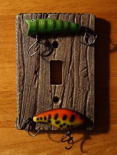 a fishing lure attached to a light switch cover on a wooden surface with a green hook