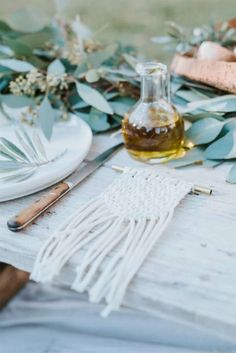 the table is set with white plates, silverware and greenery on top of it