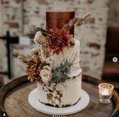 a wedding cake decorated with flowers and feathers on top of a wooden table next to a candle