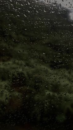 rain drops on the window as it is raining in an open field with green grass