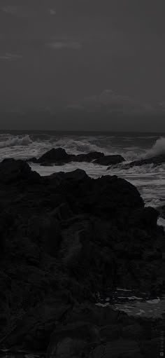 black and white photograph of waves crashing on rocks at the ocean's edge with dark sky in background