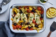 a casserole dish with chicken, tomatoes, olives and lemon wedges