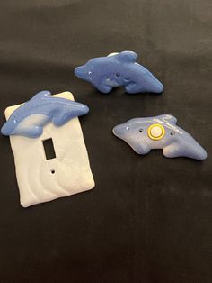 three blue and white dolphin light switch covers on a black tablecloth with a yellow button in the middle