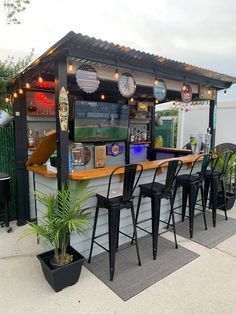 an outdoor bar with stools and lights on the outside wall, next to potted plants