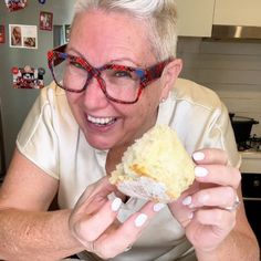 an older woman with glasses eating a piece of cake in her hands and smiling at the camera