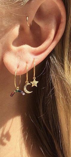 a woman wearing gold hoop earrings with stars and moon charms on it's ear