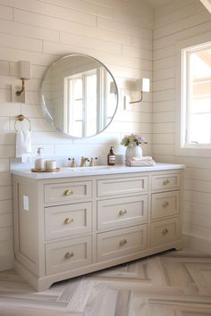 a bathroom with two sinks and a large round mirror above the sink, along with other white cabinets