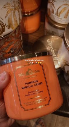 a hand holding an orange candle in front of some other candles on a counter top