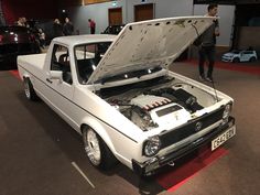 a white car with its hood open on display at an auto show in a building