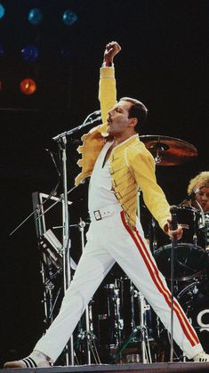 a man in yellow jacket and white pants on stage with drum set next to him