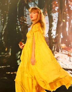 a woman in a yellow dress is walking through the woods with her hand on her hip