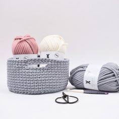 two balls of yarn are in a basket next to scissors and knitting needles on a white background