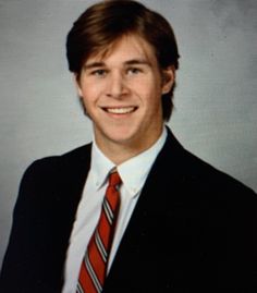 a man in a suit and tie smiling at the camera while wearing a white shirt and red striped tie