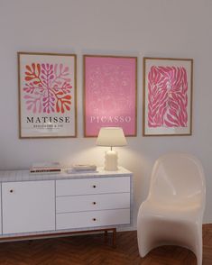 a white chair sitting next to a table with a lamp on it in front of two paintings