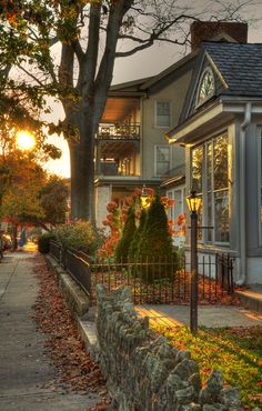 the sun is setting behind a house with many trees and bushes in front of it