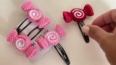 two crocheted hair clips with pink and white flowers on them, being held by someone's hand