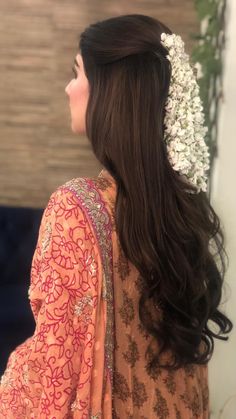 a woman with long brown hair wearing a flower in her hair and an orange dress