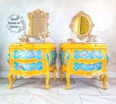 two yellow dressers with blue and gold paint on them, one has a mirror above it