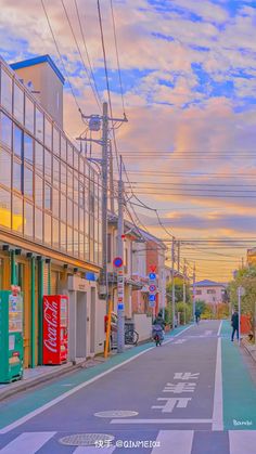 an empty street with buildings and people walking on the side walk at sunset or dawn