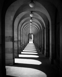 an arched walkway with light coming through the end and shadows on the ground below it