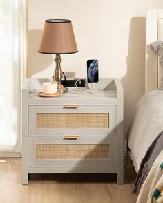 a nightstand with a cell phone on it next to a night stand and lamp in a bedroom