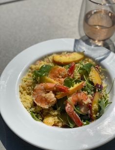 a white plate topped with shrimp and veggies next to a glass of wine