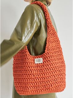 an orange crocheted bag hanging from a woman's shoulder with the tag on it