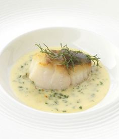 a white plate topped with scallops covered in sauce and garnished with herbs