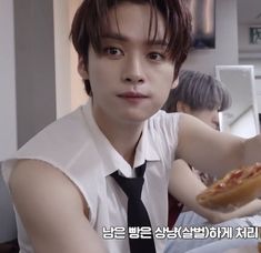 a young man in a white shirt and black tie is eating pizza at a table