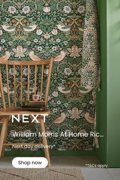 a wooden chair sitting in front of a green wall with a bird pattern on it