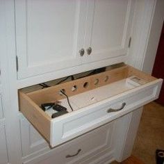 a kitchen with white cupboards and an open drawer in the middle that is filled with tools