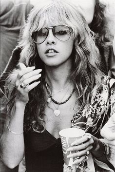 a black and white photo of a woman with sunglasses on holding a drink in her hand