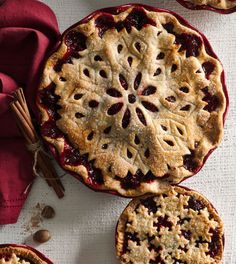 three pies on top of a white table with red cloth and cinnamon sticks next to them