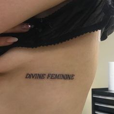 a woman's stomach with the word divine feminine tattooed on her lower back side