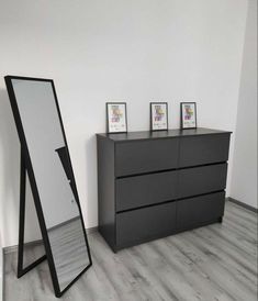 a large mirror sitting on top of a dresser next to a tall black cabinet with three pictures