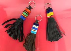 two tasseled keychains on a pink background one has a multi - colored beaded tassel and the other has a black leather tassel