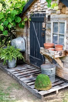 an old wooden shed with potted plants on the porch