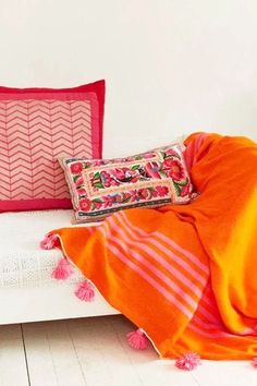 an orange and pink blanket sitting on top of a white couch next to two pillows