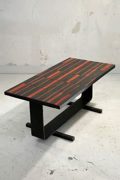 a wooden table with black legs and an orange stripe design on the top, against a white background