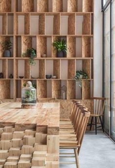 a wooden table surrounded by chairs and shelves with plants on them in front of a window