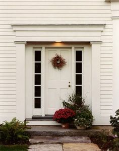 a white door with two wreaths on it and some flowers in the foreground