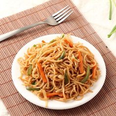 a white plate topped with noodles and veggies on top of a place mat