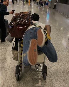 a man laying on top of a luggage cart in an airport next to other people