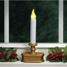 a lit candle sitting on top of a window sill next to holly wreaths