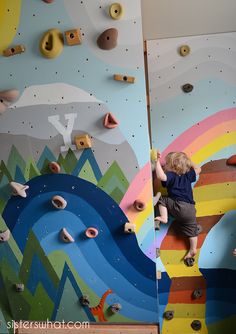 a young boy climbing up the side of a wall with colorful rocks and rainbows painted on it