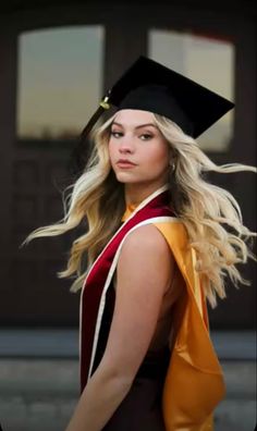 a woman in a graduation gown and cap walks down the street with her hair blowing in the wind