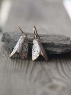 two white and gold earrings sitting on top of a piece of wood