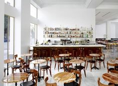 an empty restaurant with wooden tables and chairs in front of a bar filled with bottles