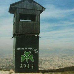 a wooden clock tower on top of a hill with graffiti written on the side and below it